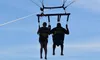 Two people are parasailing over the ocean with a colorful parachute against a clear blue sky.