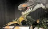 The image shows a museum exhibit featuring large dinosaur models with informational displays and plants in the background.