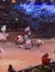 Santa Claus is riding in a horse-drawn sleigh inside an arena with people watching and a snowy, festive backdrop.