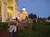 People are walking and gathering near a large, illuminated building with arches at dusk.