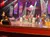 Performers are on stage under colorful lights, dressed in country-themed attire with a