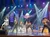 Performers in colorful, sequined outfits and cowboy hats are dancing on a stage labeled