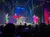 Performers in bright costumes dance energetically on a colorful stage in front of an audience.