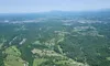 The image shows an aerial view of a landscape with lush green fields, scattered houses, and distant mountains under a clear blue sky.