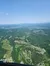 The image shows an aerial view of a landscape with lush green fields, scattered houses, and distant mountains under a clear blue sky.