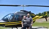 A couple is standing in front of a black and yellow helicopter on a clear day.