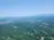 The image shows an aerial view of a vast, lush green landscape with distant mountains under a clear blue sky.