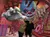 Two people pose as if being attacked by a giant, menacing clown in a cartoonish, wrecked circus setting.