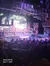 The image shows a lively indoor theater stage with a rustic, forest-themed set, an audience seated in the foreground, and several performers on stage near a small boat.