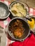 A table is set with a variety of Southern-style dishes, including fried chicken, mashed potatoes, coleslaw, corn on the cob, and drinks, all on a red checkered tablecloth.