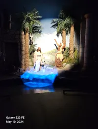 The image shows a lifelike display of two figures in biblical attire, set amidst palm trees with blue light illuminating the scene.