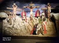 The image depicts a dramatic representation of the crucifixion scene with several figures in historical attire surrounding three crosses on a rocky backdrop.