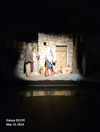 The image shows a nativity scene with figures dressed in robes standing outside a rustic stone building.