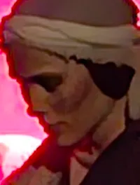 A person in a headscarf is sitting on a rocky ledge near a glowing pink-lit opening.