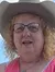 A person wearing a cowboy hat and a pink dress is sitting on a stationary horse figure outdoors under a blue sky.