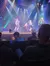 Performers are energetically dancing on a well-lit stage with colorful lighting effects in front of an audience.