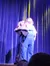 A person in overalls is performing with a puppet on a stage with a blue curtain backdrop.