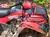 A red Brute Force 300 ATV is parked outdoors on a dirt and leaf-covered ground.