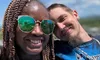 Two people are smiling together, wearing matching Great Smoky Mountains shirts, with a clear blue sky in the background.