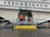 Three people are standing in front of a building designed to appear upside down, with