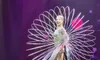 A performer in a shimmering costume poses with a circular, wire-like apparatus on a stage illuminated by purple lights.