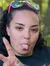 A person is sitting on a red ATV in a wooded area, making a peace sign gesture and sticking out their tongue.