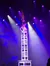 A performer is balancing upside down on a tall stack of chairs under dramatic stage lighting.