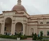 Three people are standing in front of a building with large arches, next to a lion sculpture on a rock display.