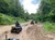A group of people are riding ATVs on a muddy trail surrounded by lush greenery.