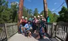 A group of people wearing helmets and harnesses are gathered on a wooden platform, smiling and posing for the photo, likely before ziplining in a forested area.