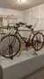 The image shows a vintage bicycle with bamboo supports on display in a museum exhibit.