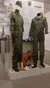 The image shows a museum display with military uniforms, a guitar, folded American flag, and various medals and documents.