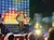 A performer with a guitar is on stage under colorful lights, entertaining a seated audience.