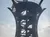 The image shows a tall, modern observation tower with a spiral staircase and triangular shade structures at the top, silhouetted against a cloudy sky.