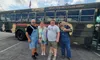 Four people are standing in front of a camo-colored bus labeled 