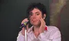 A person is performing on stage with a microphone, wearing a white shirt and black hair styled in curls.