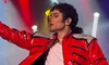 A performer wearing a shiny red jacket and white shirt is on stage with colorful lights in the background.