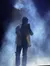 A performer is singing on stage amidst a dramatic cloud of smoke, illuminated by blue light.