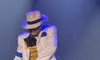 A performer wearing a fedora and stylish outfit dances energetically on stage under blue lighting.