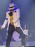 A performer wearing a fedora and stylish outfit dances energetically on stage under blue lighting.