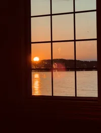 A sunset is visible through a window with grid panes, casting a warm glow over a body of water.