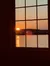 A sunset is visible through a window with grid panes, casting a warm glow over a body of water.
