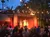 A crowd watches a traditional dance performance on an outdoor stage decorated with string lights and surrounded by palm trees.