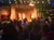 A group of people is watching a traditional Polynesian dance performance outdoors under string lights in the evening.