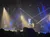 A live band performs on stage under vibrant, colorful stage lights with an audience visible in the foreground.