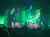 A vibrant stage performance is taking place with dynamic lighting and a large screen displaying colorful visuals in front of a seated audience.