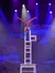 An acrobat performs a handstand on top of a tall stack of chairs under stage lighting.
