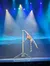 A performer balances on a long pole during a stage performance, illuminated by colorful spotlights.