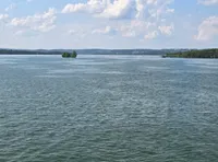 The image shows a serene body of water under a blue sky with scattered clouds and a distant shoreline.