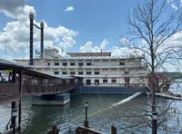 A large riverboat is docked beside a wooden walkway on a sunny day with a partly cloudy sky.